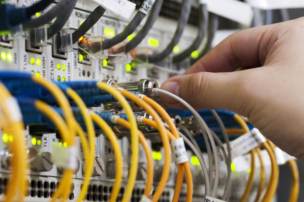 Hand Plugging a Fiber Optic Cable Into a Server Rack, With Orange and Yellow Cables — Micromac Computers in Charmhaven, NSW