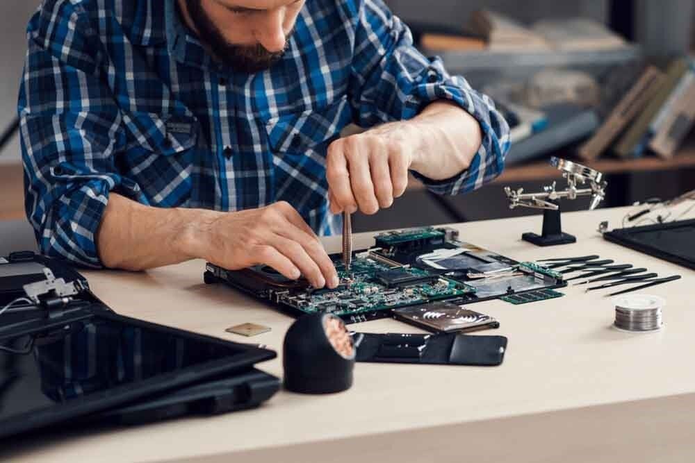 Man in Blue Plaid Shirt Repairing a Circuit Board With Tools on a Desk — Micromac Computers in Charmhaven, NSW
