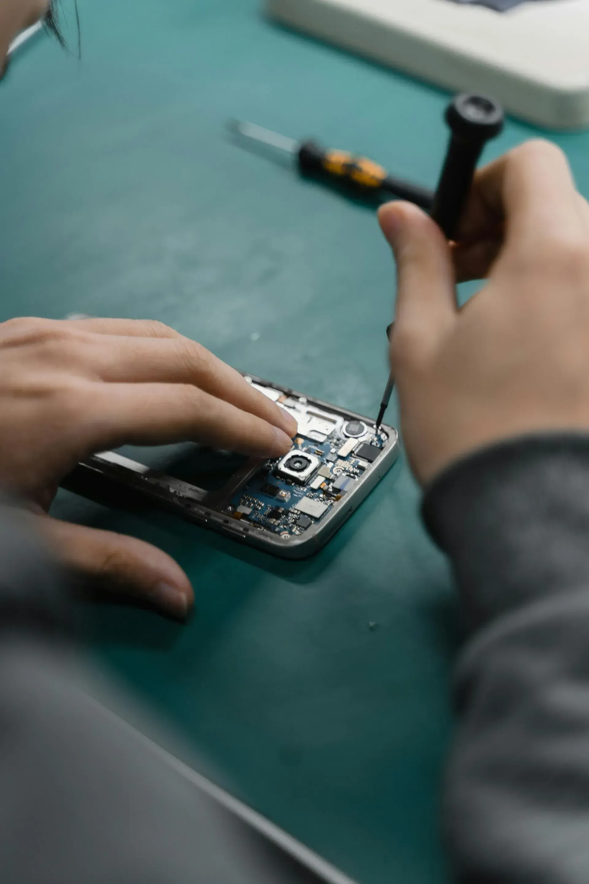 Person Disassembling a Cell Phone With Tools on a Green Surface — Micromac Computers in Charmhaven, NSW