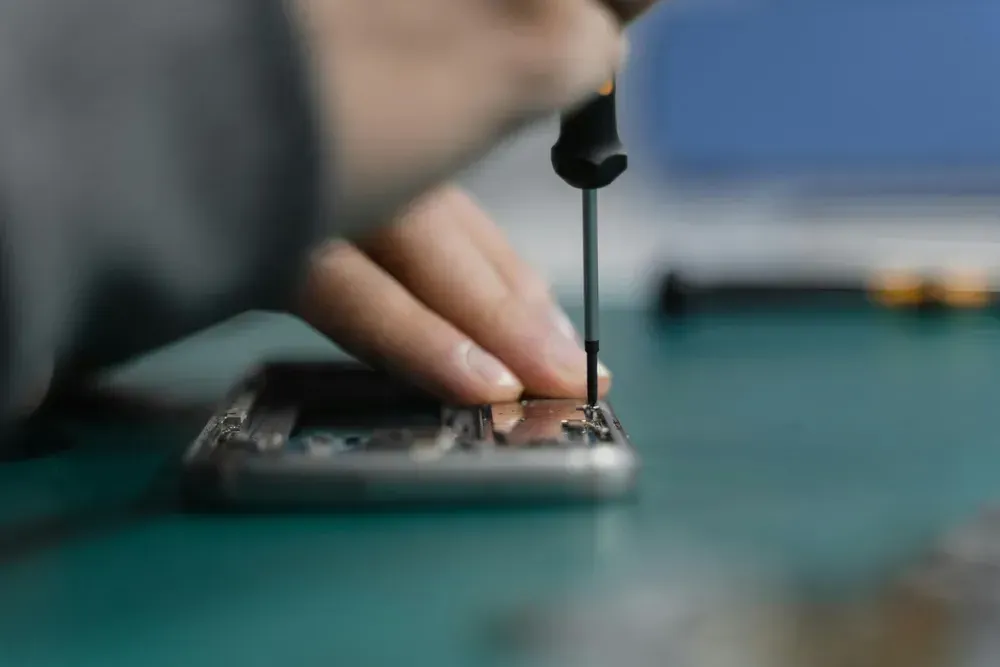 Person Using a Screwdriver to Repair a Smartphone on a Teal Surface — Micromac Computers in Charmhaven, NSW