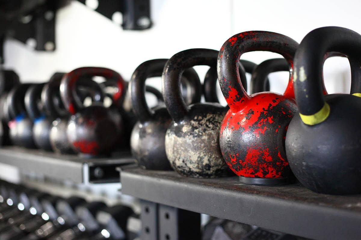 A row of kettlebells are lined up on a shelf in a gym.
