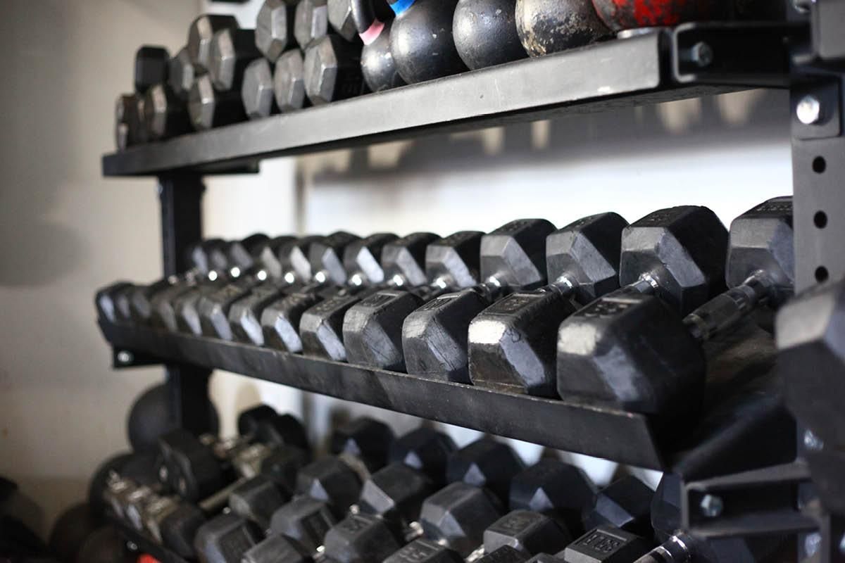 A shelf filled with dumbbells and kettlebells in a gym.