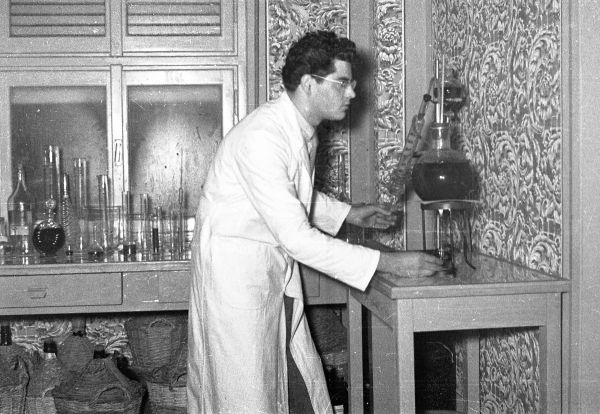 Uomo in camice in un laboratorio, al lavoro con vetreria e attrezzature.