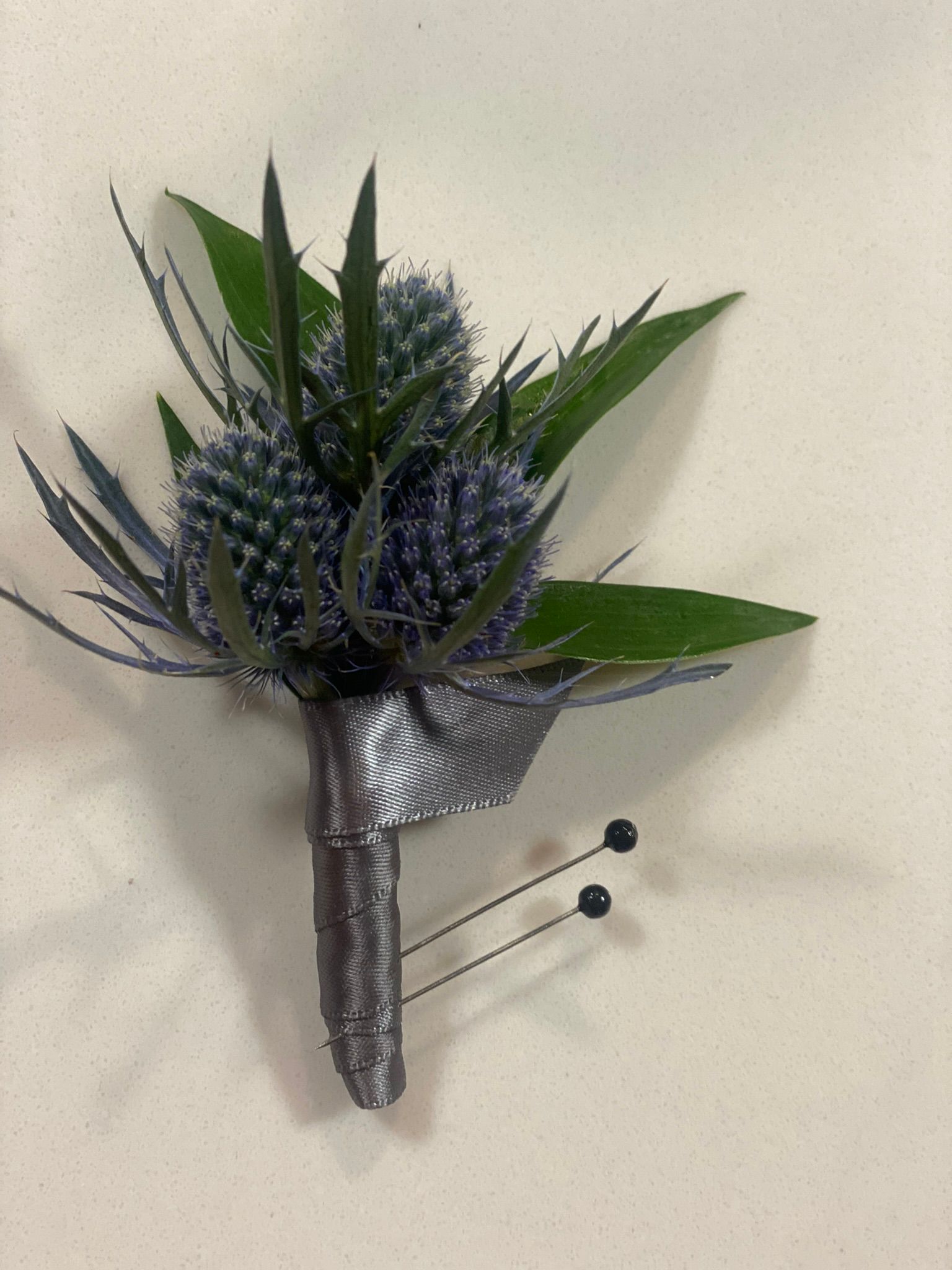A buttonhole with a purple flower and green leaves on a white surface.