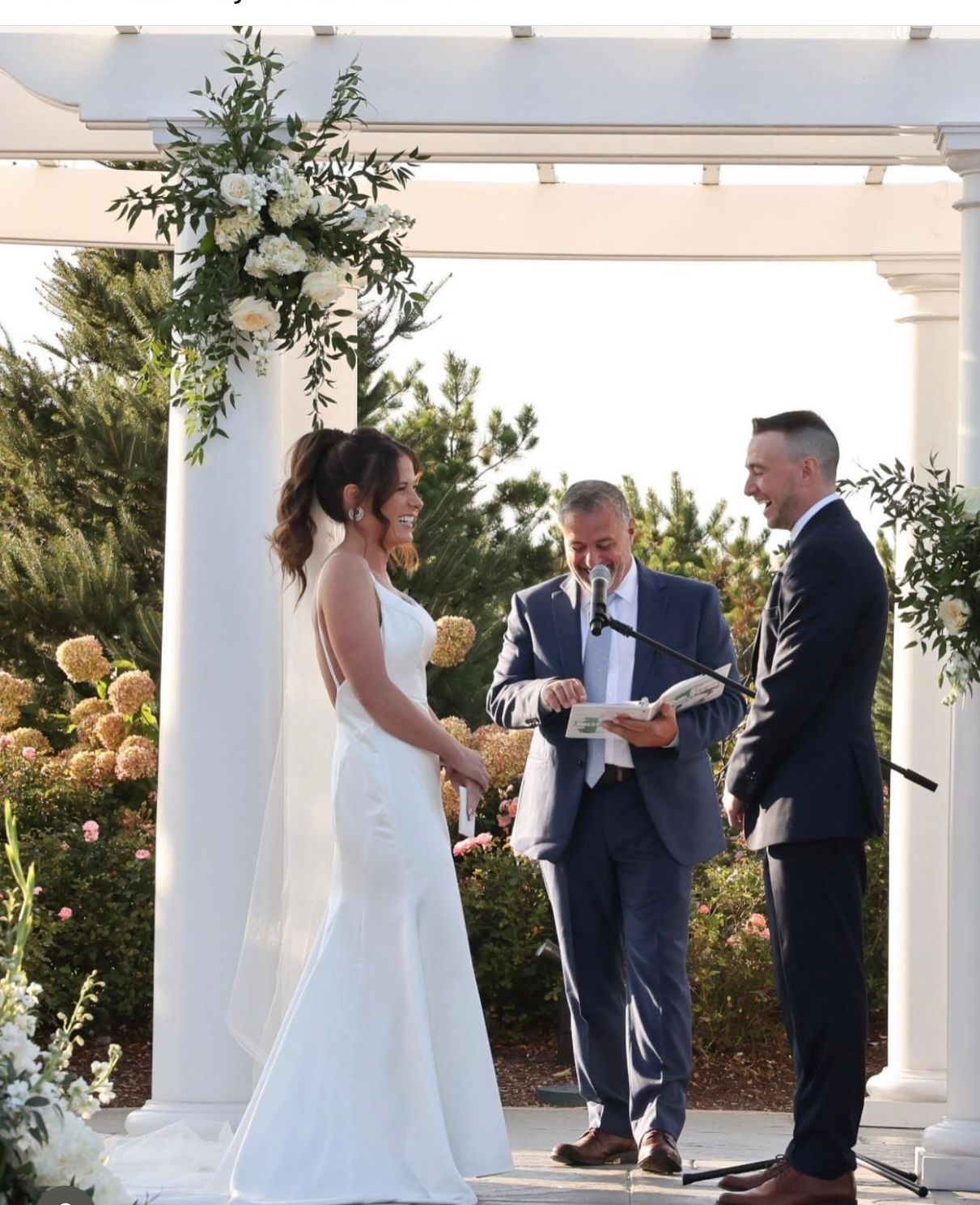 A bride and groom are getting married under a white pergola