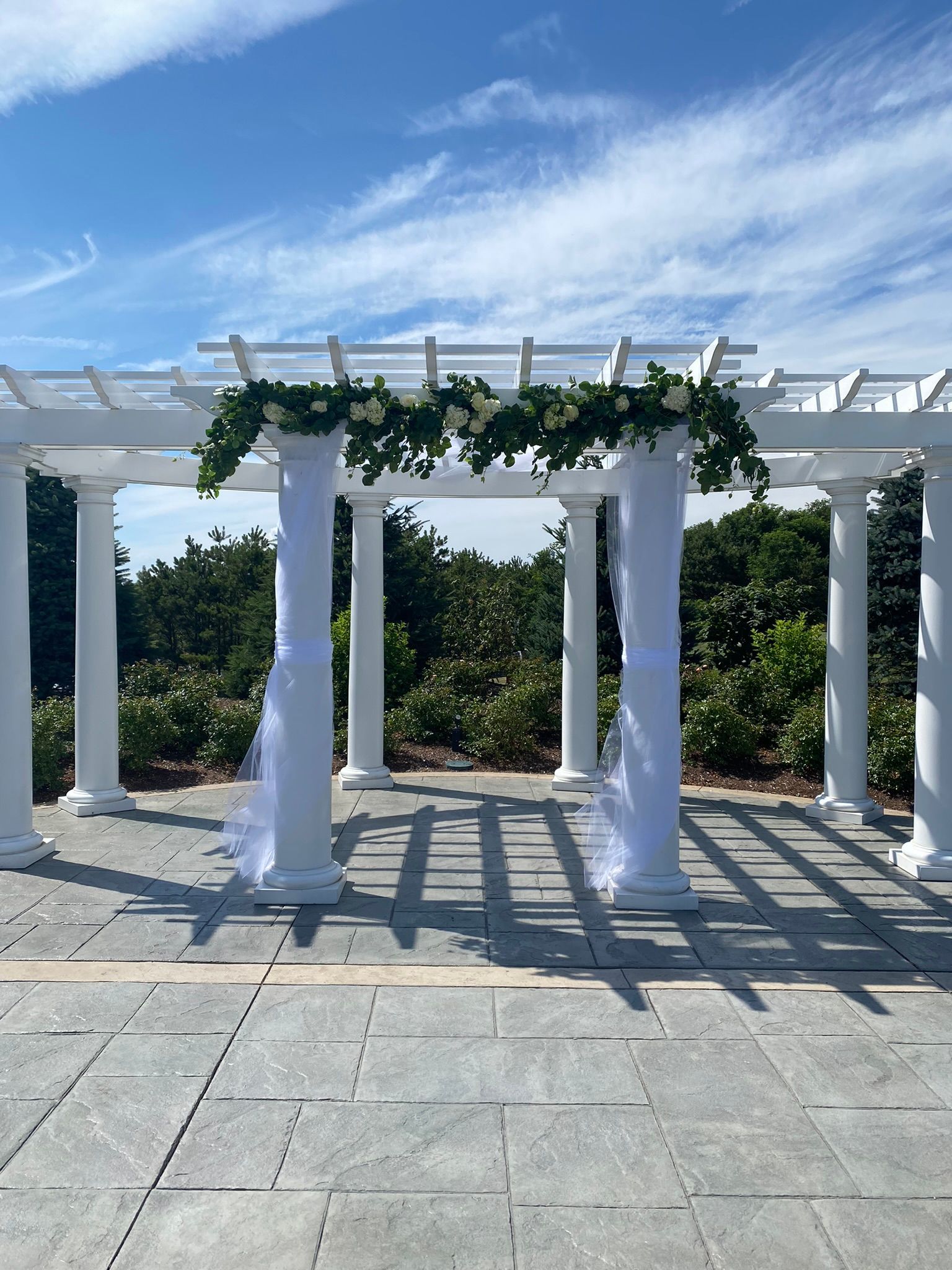 A white pergola with columns and flowers on it