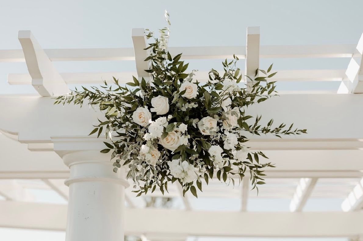 A white pergola with white flowers and greenery hanging from it.