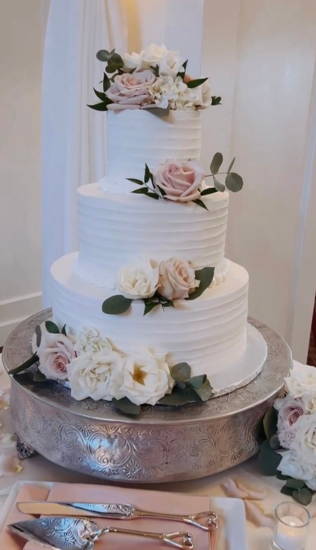 A wedding cake is sitting on top of a silver cake stand on a table.