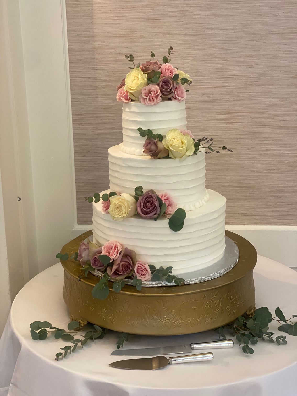 A wedding cake is sitting on top of a gold cake stand on a table.