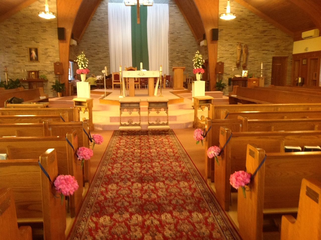 The inside of a church decorated for a wedding with pink flowers on the benches.