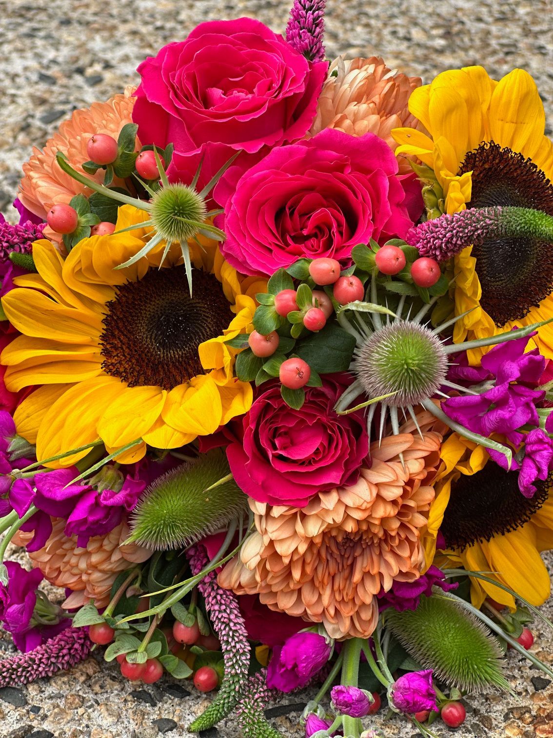 A close up of a bouquet of flowers with sunflowers , roses , and other flowers.