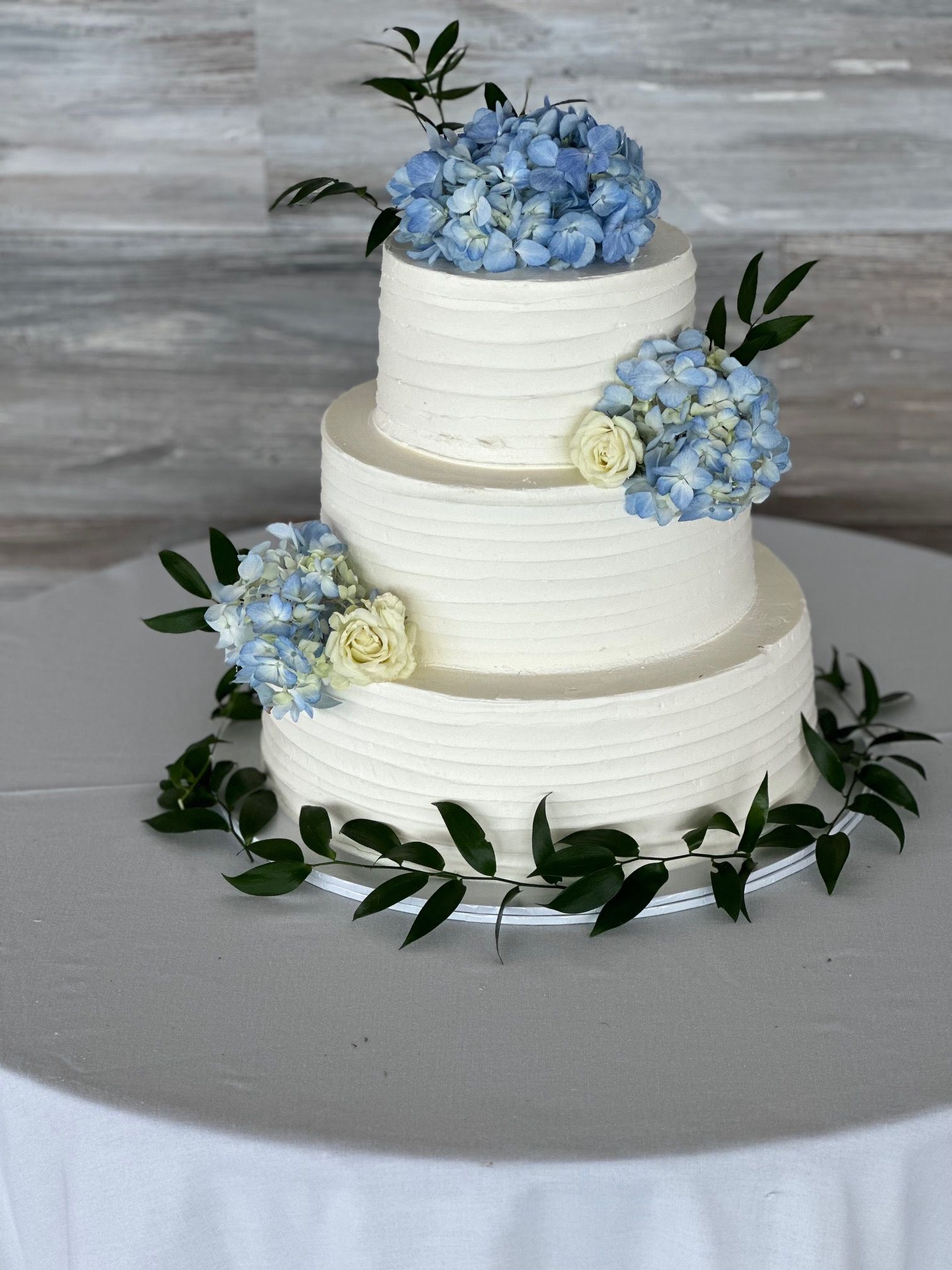 A white wedding cake with blue flowers and leaves on a table.