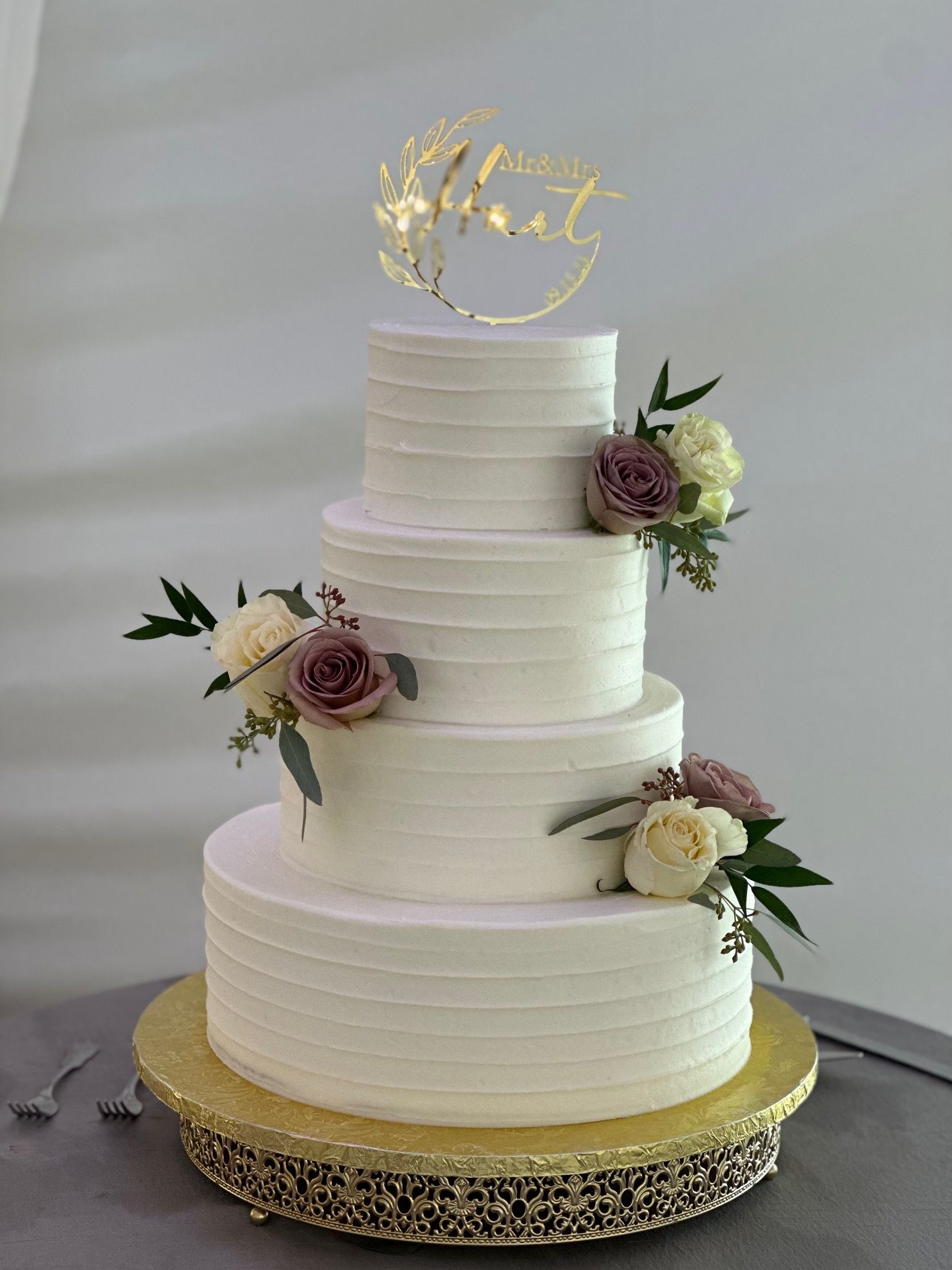 A white wedding cake with flowers on it is sitting on top of a gold cake stand.