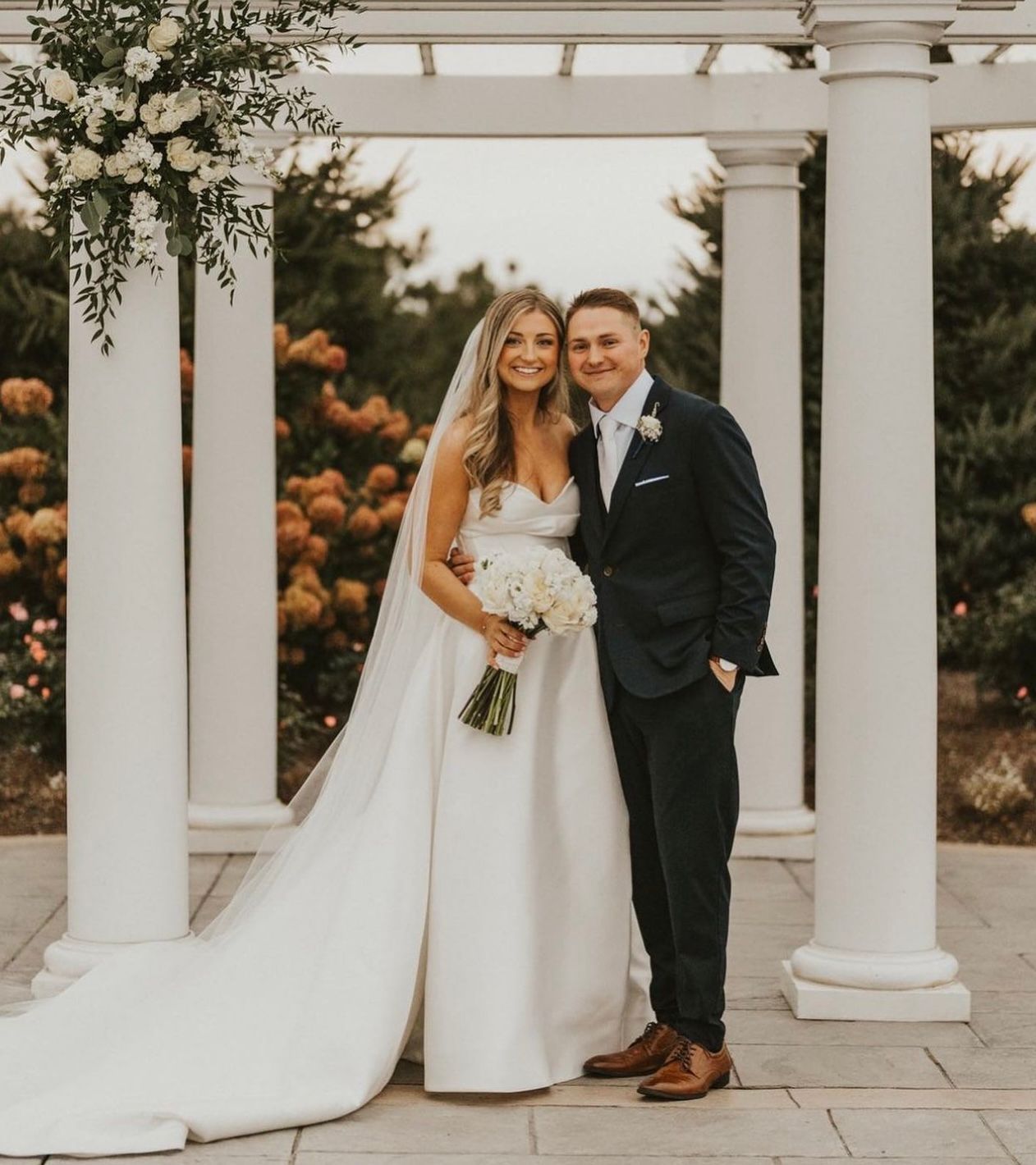 A bride and groom pose for a picture under a pergola