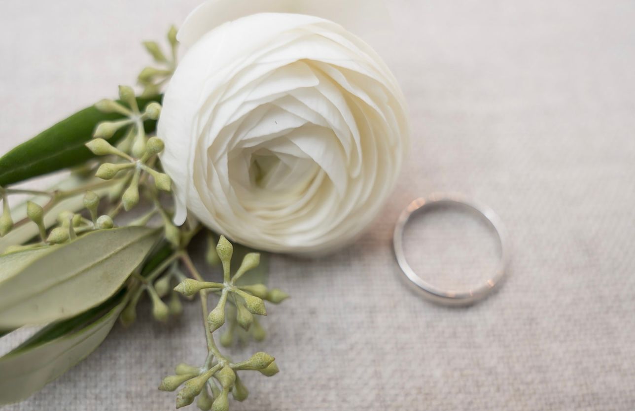 A white rose and two wedding rings are on a table.