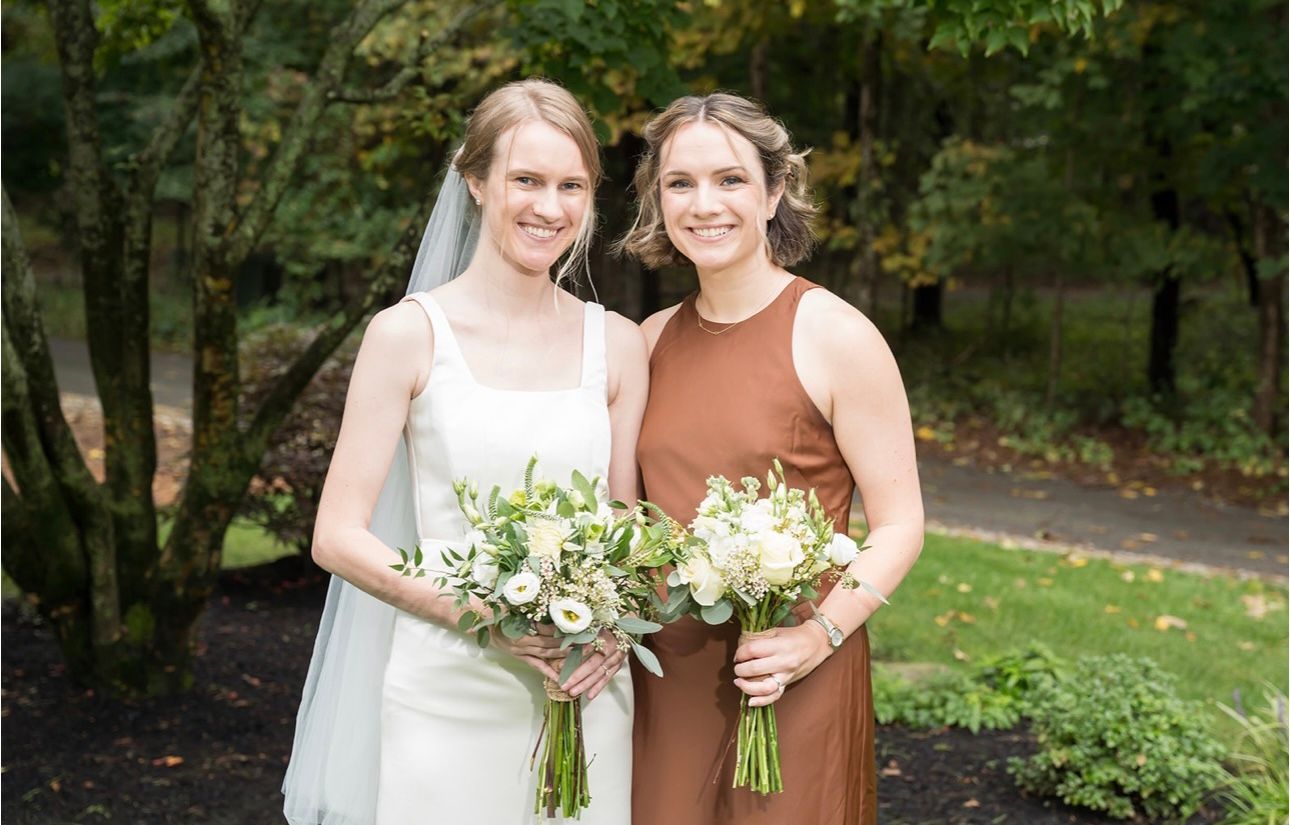 A bride and her bridesmaid are posing for a picture while holding bouquets of flowers.