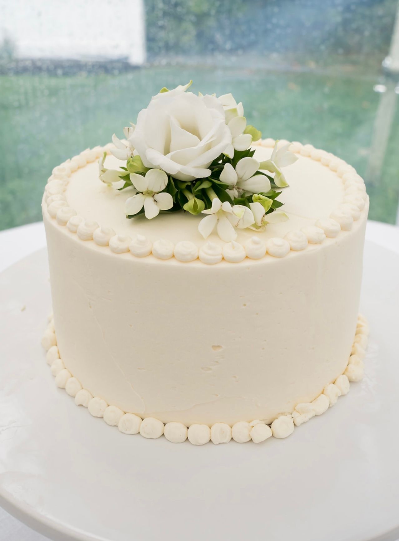 A white cake with a white rose on top is on a white plate.