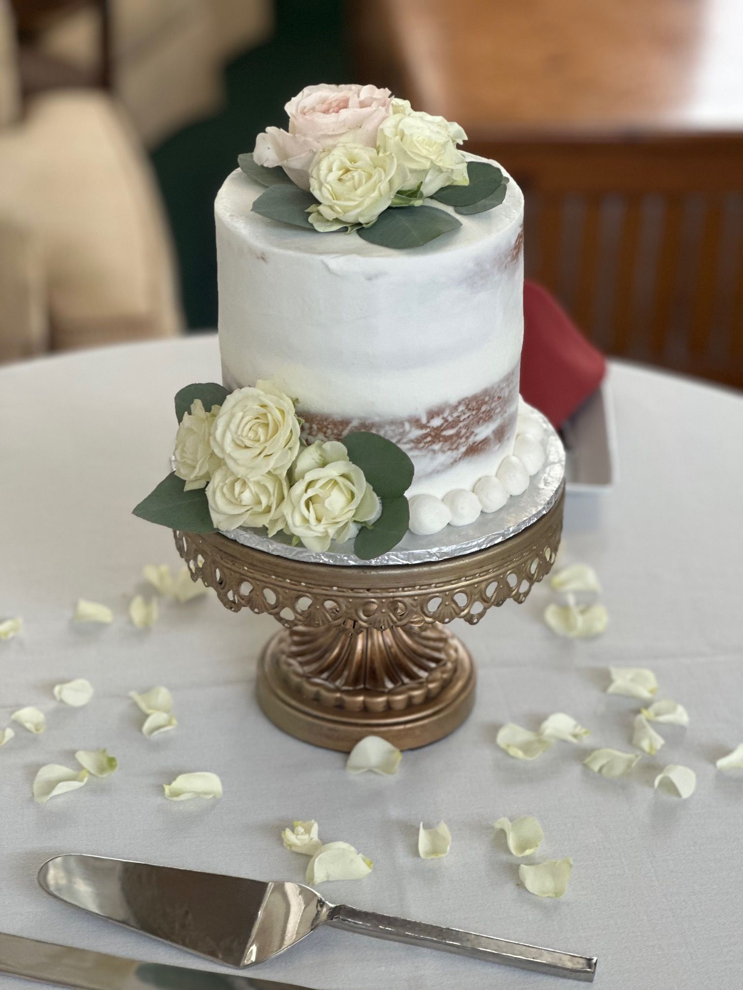 A small wedding cake on a gold cake stand on a table.