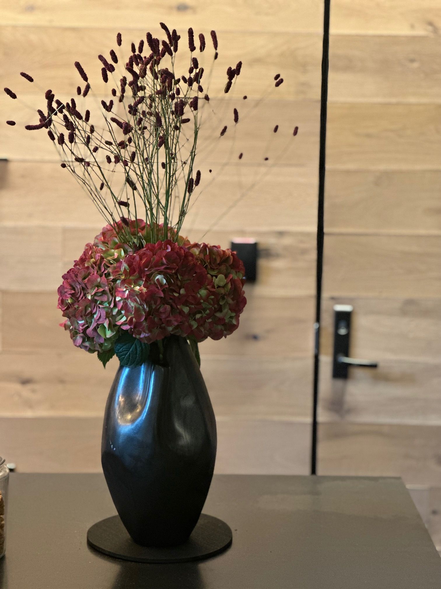 A black vase filled with red flowers sits on a table