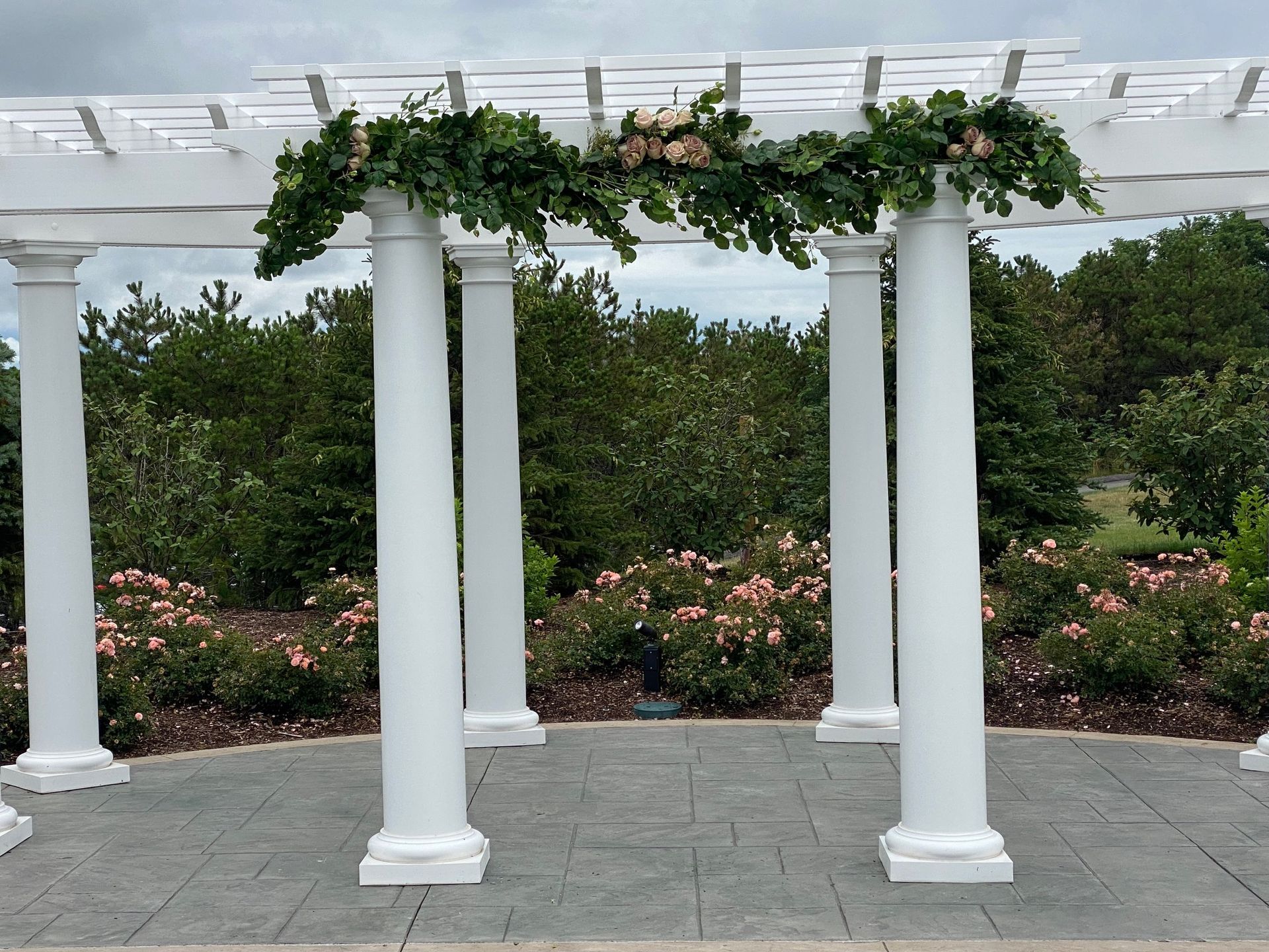 A white pergola with columns and flowers hanging from it.