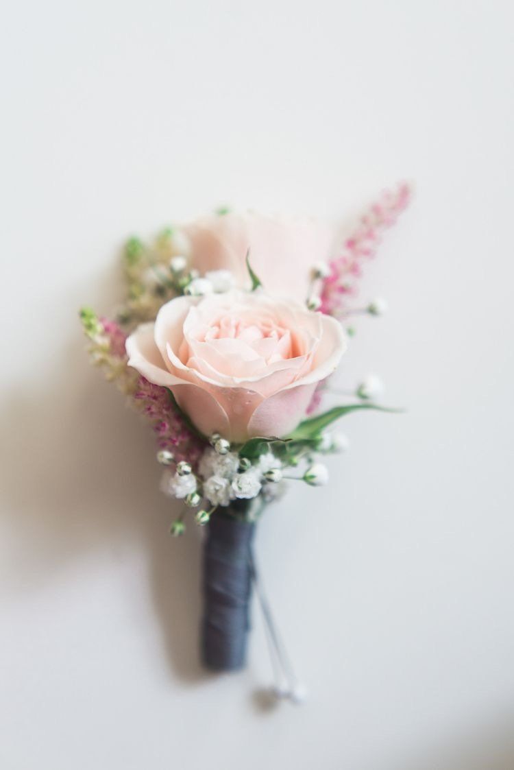 A close up of a buttonhole with a pink rose and baby 's breath.