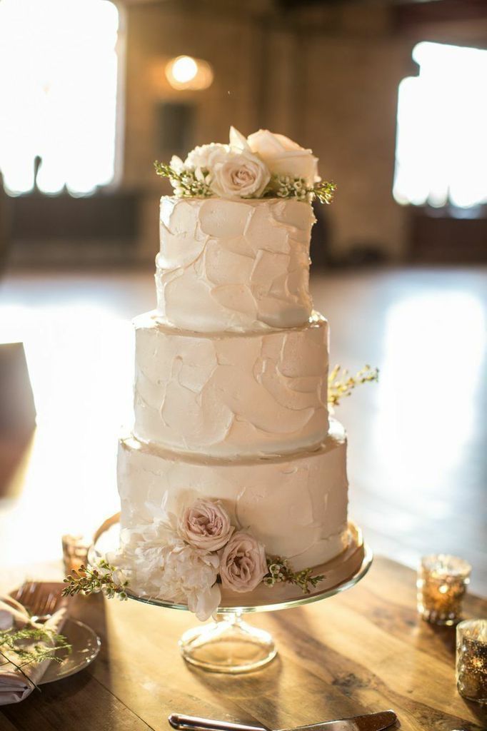 A white wedding cake is sitting on top of a wooden table.