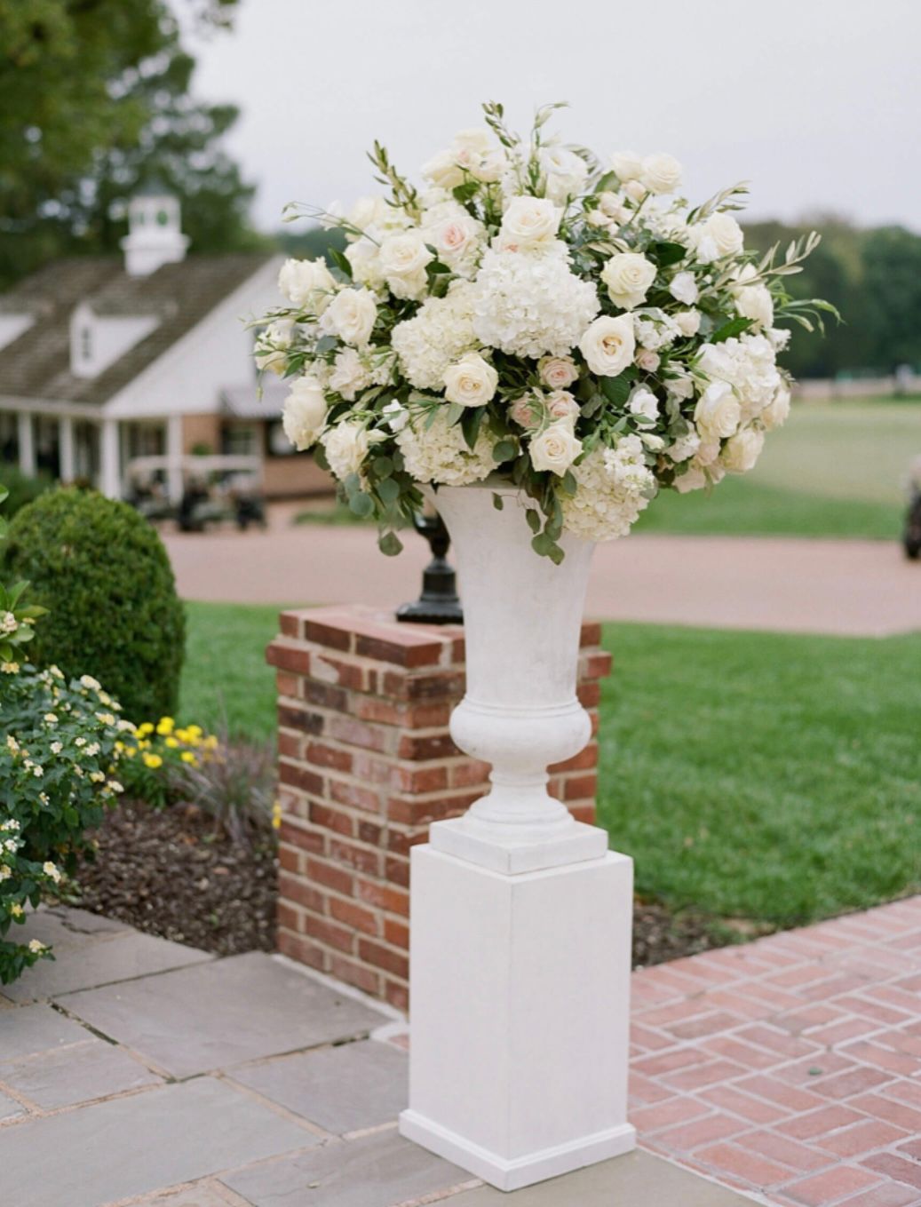 A white vase filled with white flowers is sitting on a white pedestal.