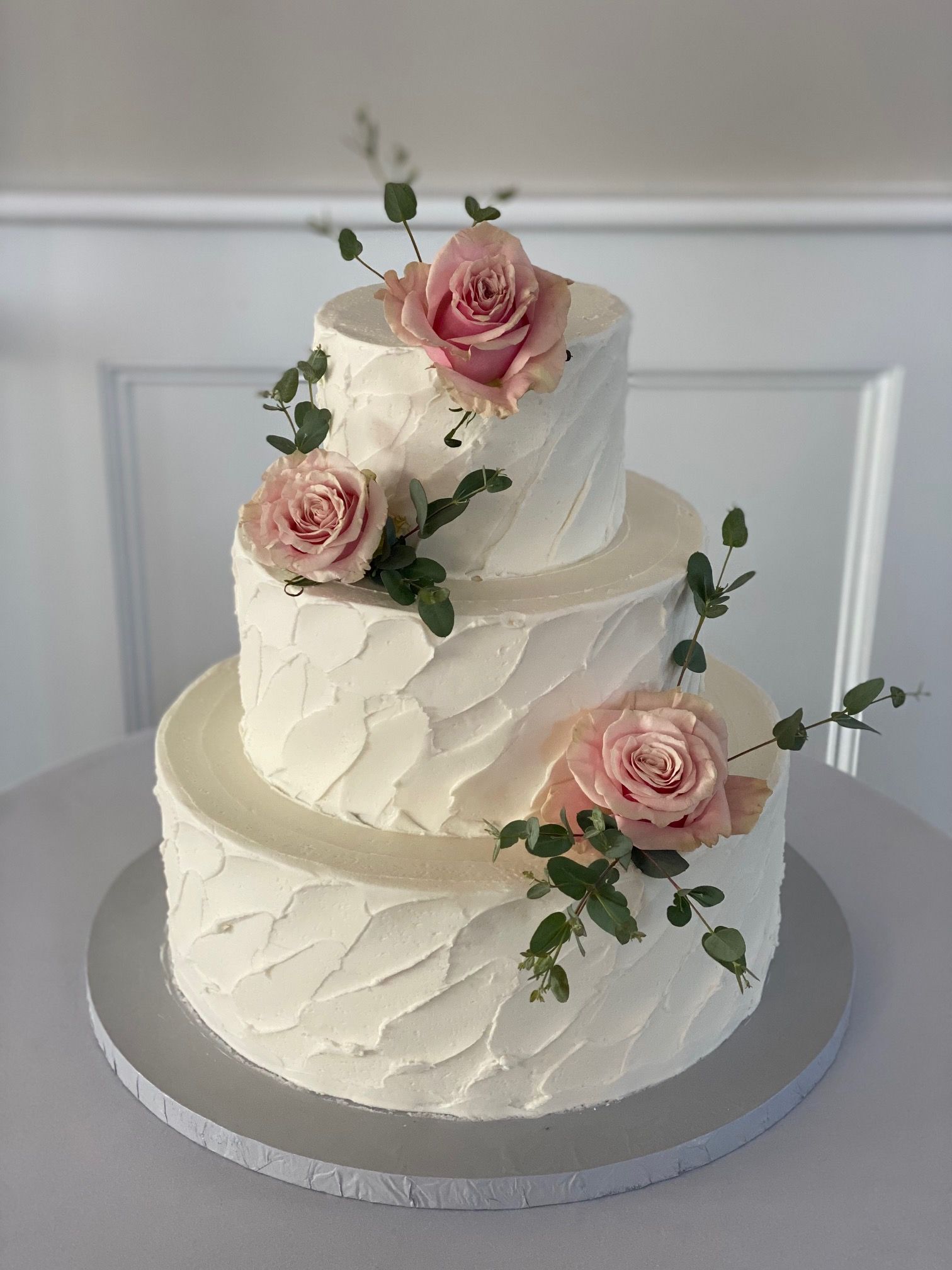A white wedding cake with pink roses on top is sitting on a table.