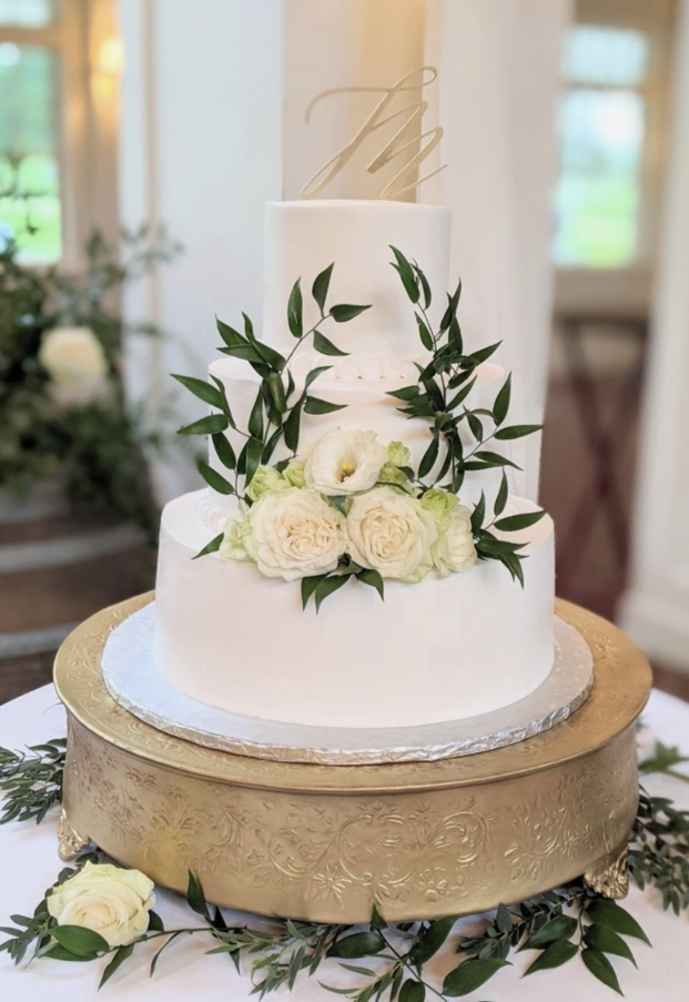 A wedding cake is sitting on top of a gold cake stand on a table.