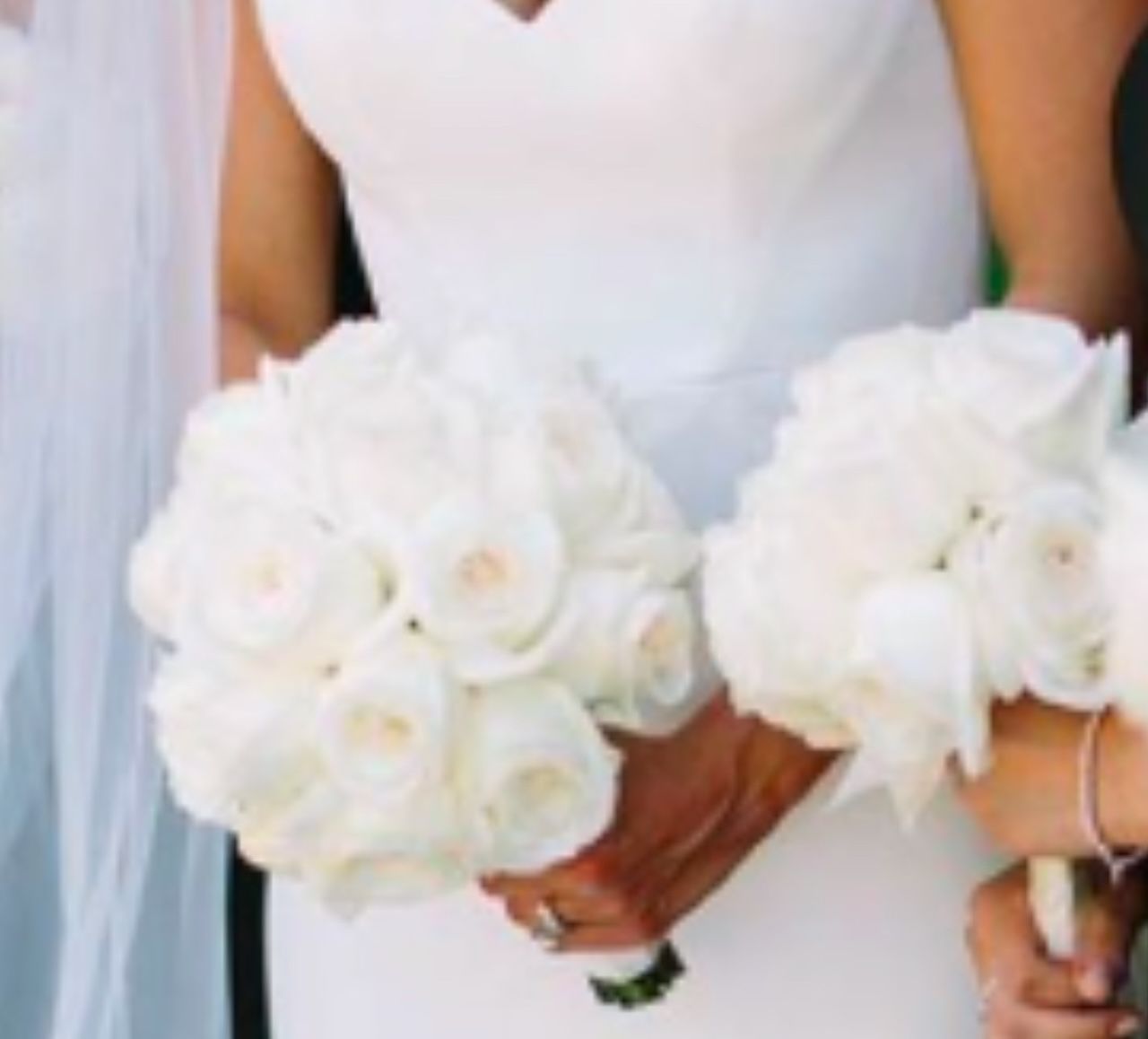 A bride in a white dress is holding a bouquet of white roses
