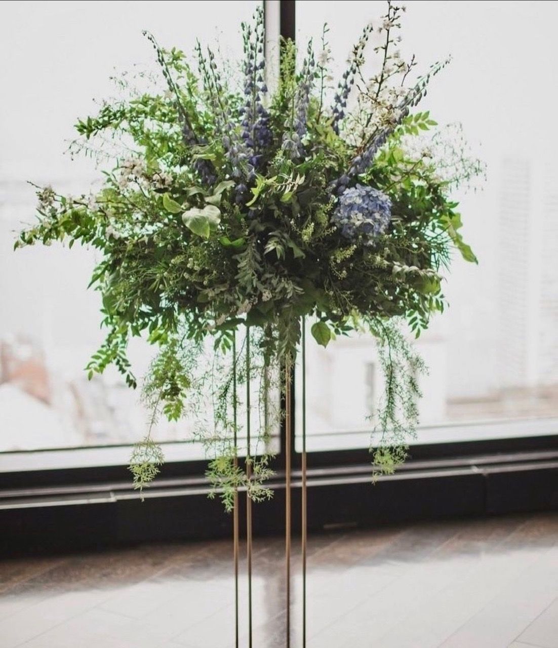 A large bouquet of flowers is sitting on a metal stand in front of a window.
