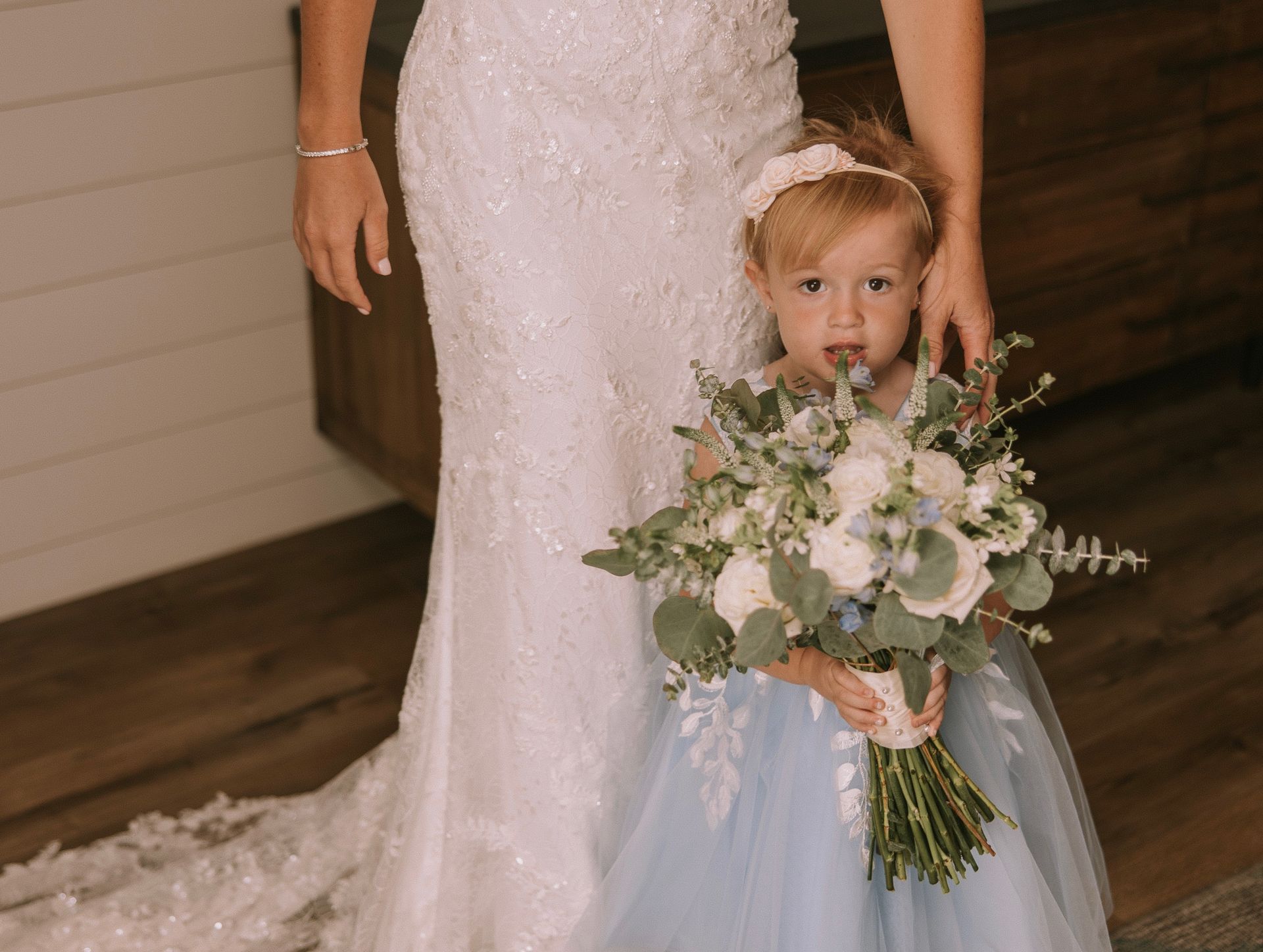 A little girl in a blue dress is holding a bouquet of flowers next to a bride in a wedding dress.