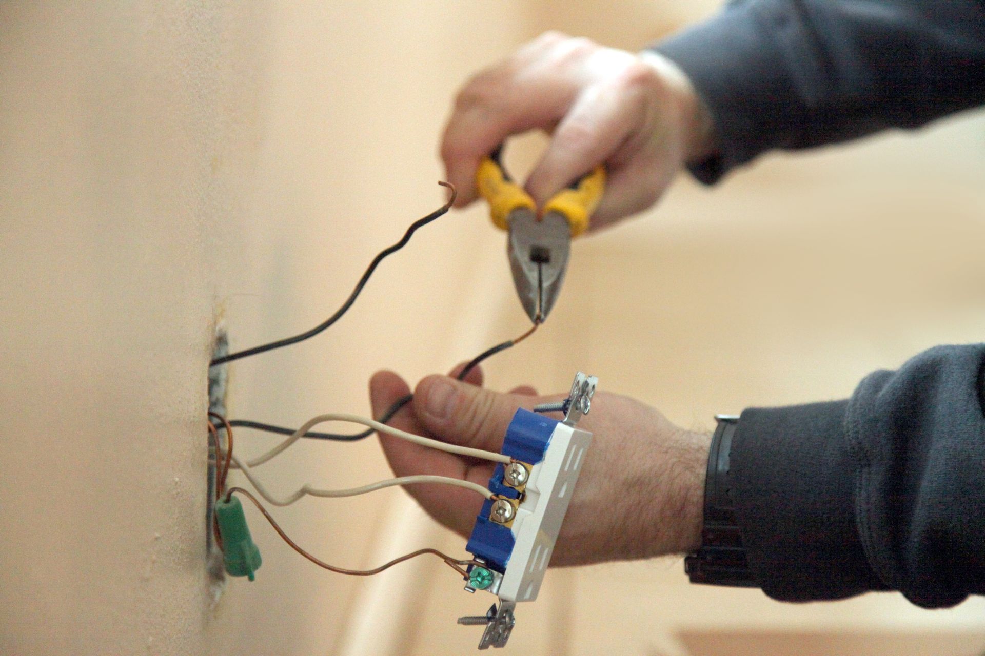 A man is working on an electrical outlet with a screwdriver.