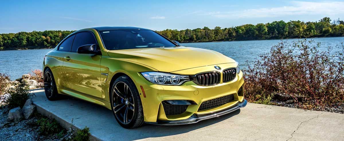 Austin Yellow bmw M4 with carbon fiber front lip spoiler is parked next to a lake