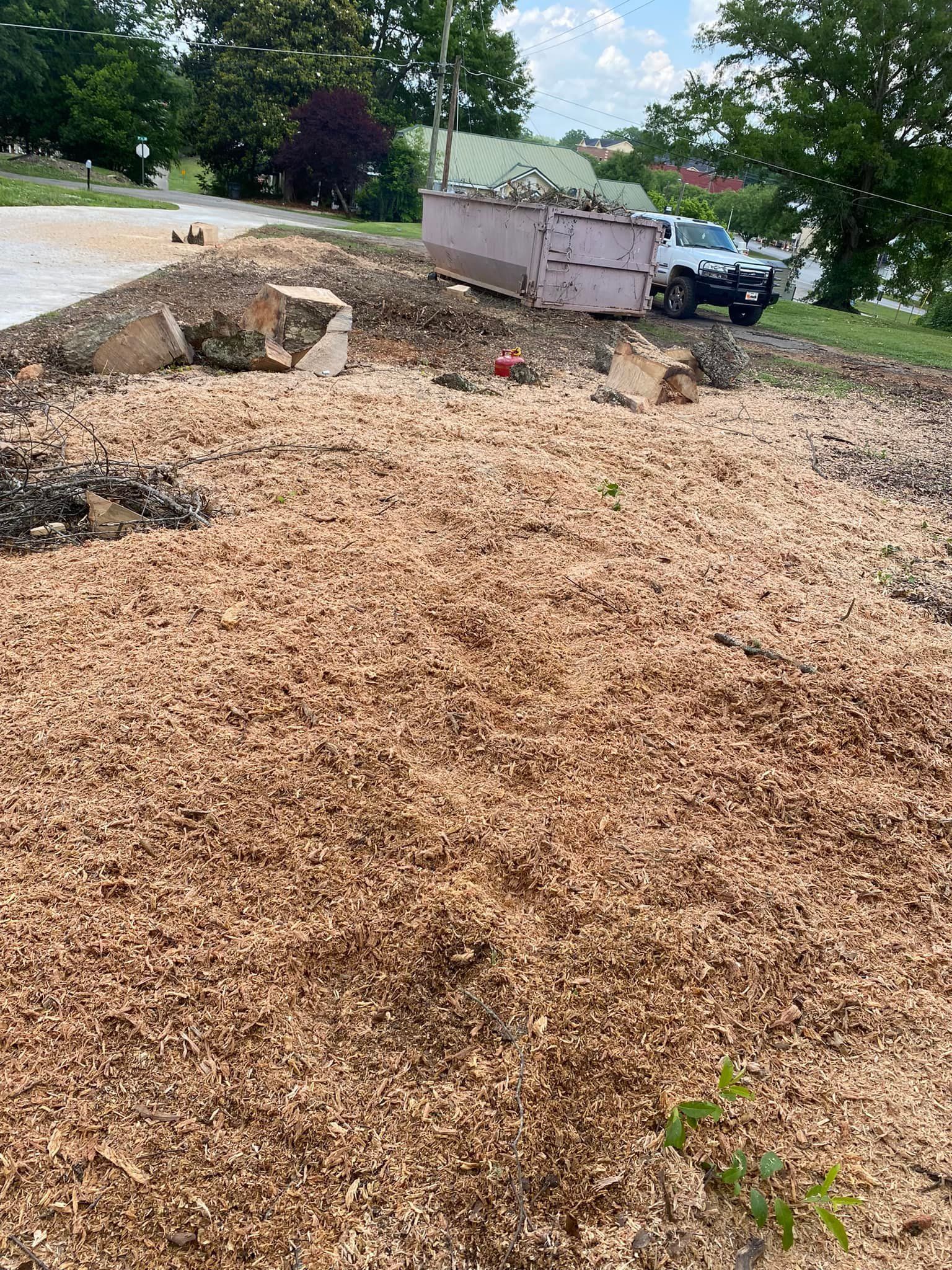 A pile of wood chips in a yard with a dumpster in the background.