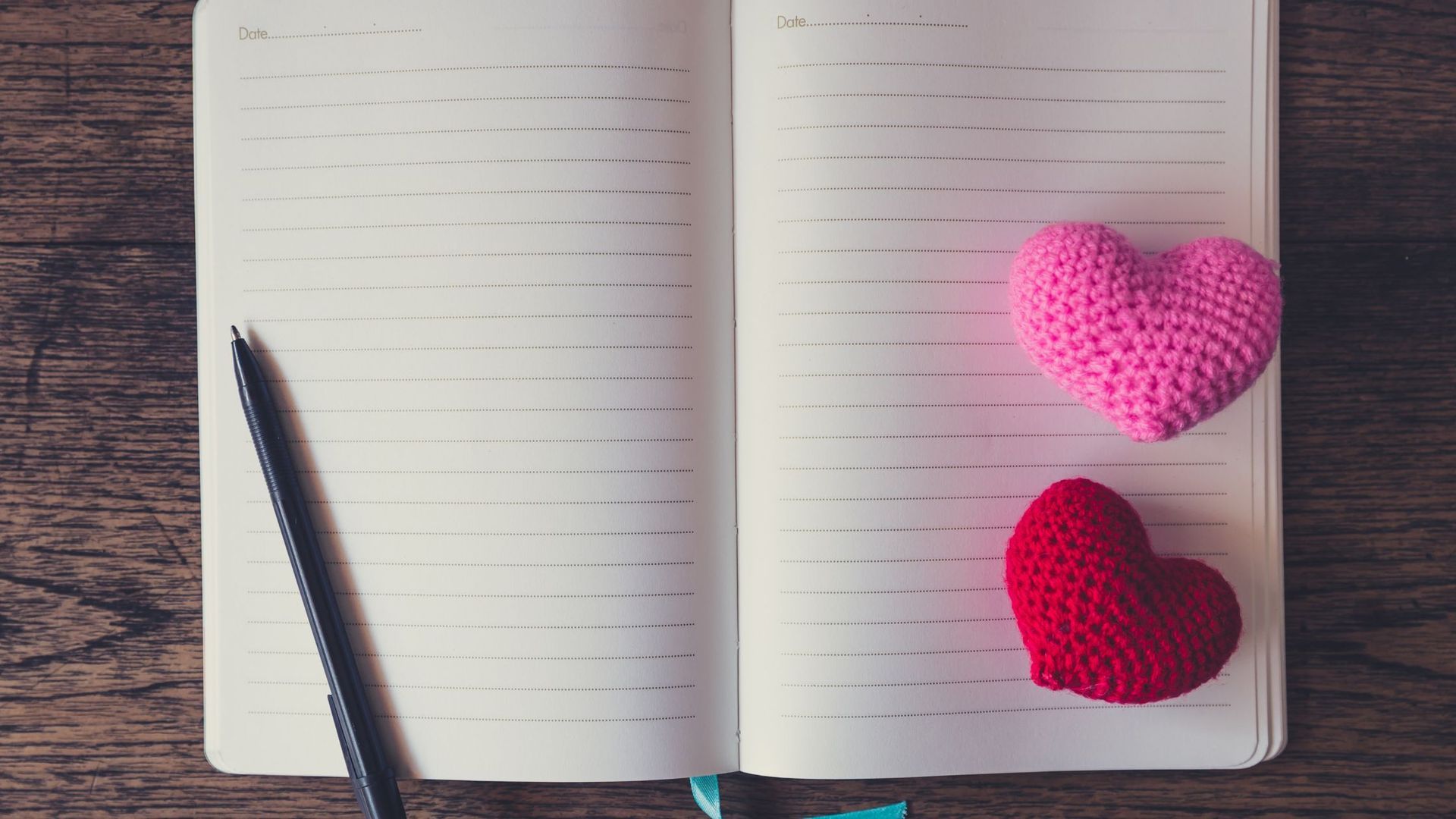 open book with a pen and two crocheted hearts