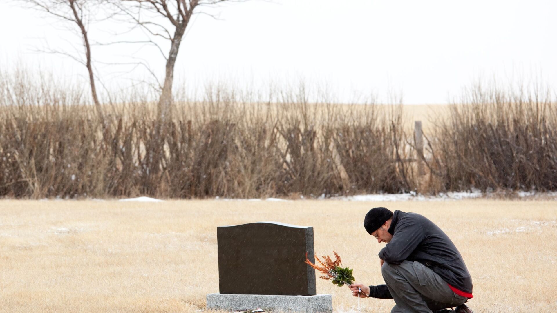 Elderly gentleman sitting at a loved ones grave putting flowers on the grave
