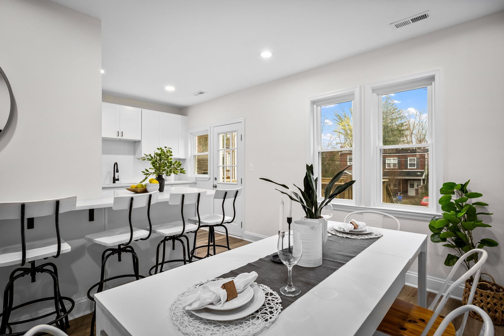 A dining room with a table and chairs and a kitchen in the background.
