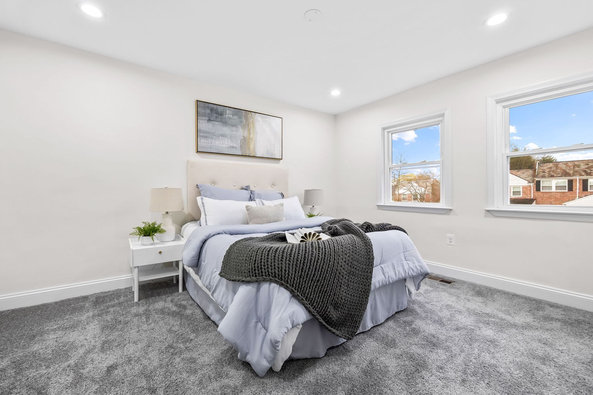 A bedroom with a bed , nightstand , and two windows.