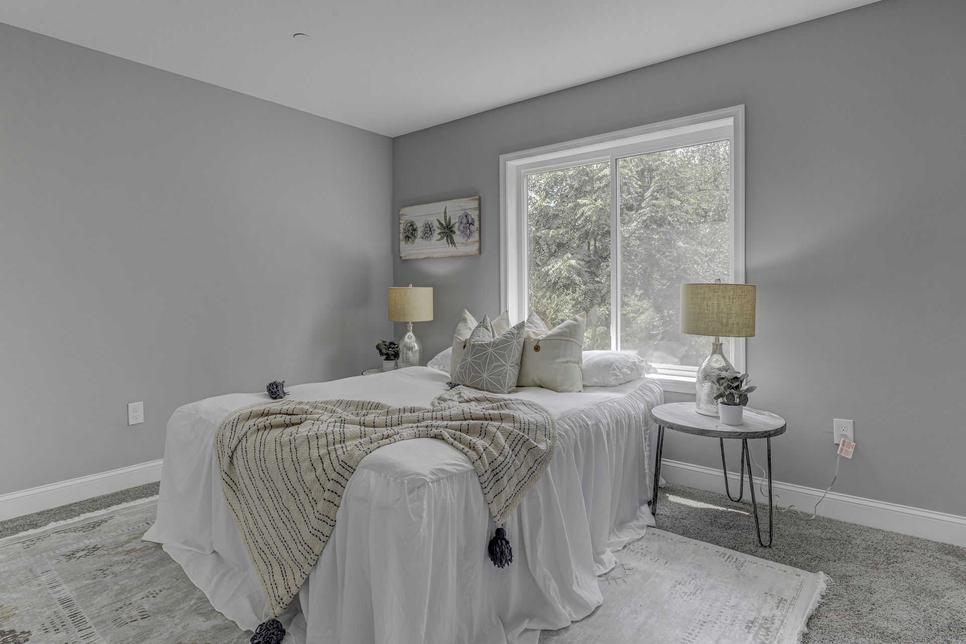 A bedroom with a bed , two lamps , a table and a window.