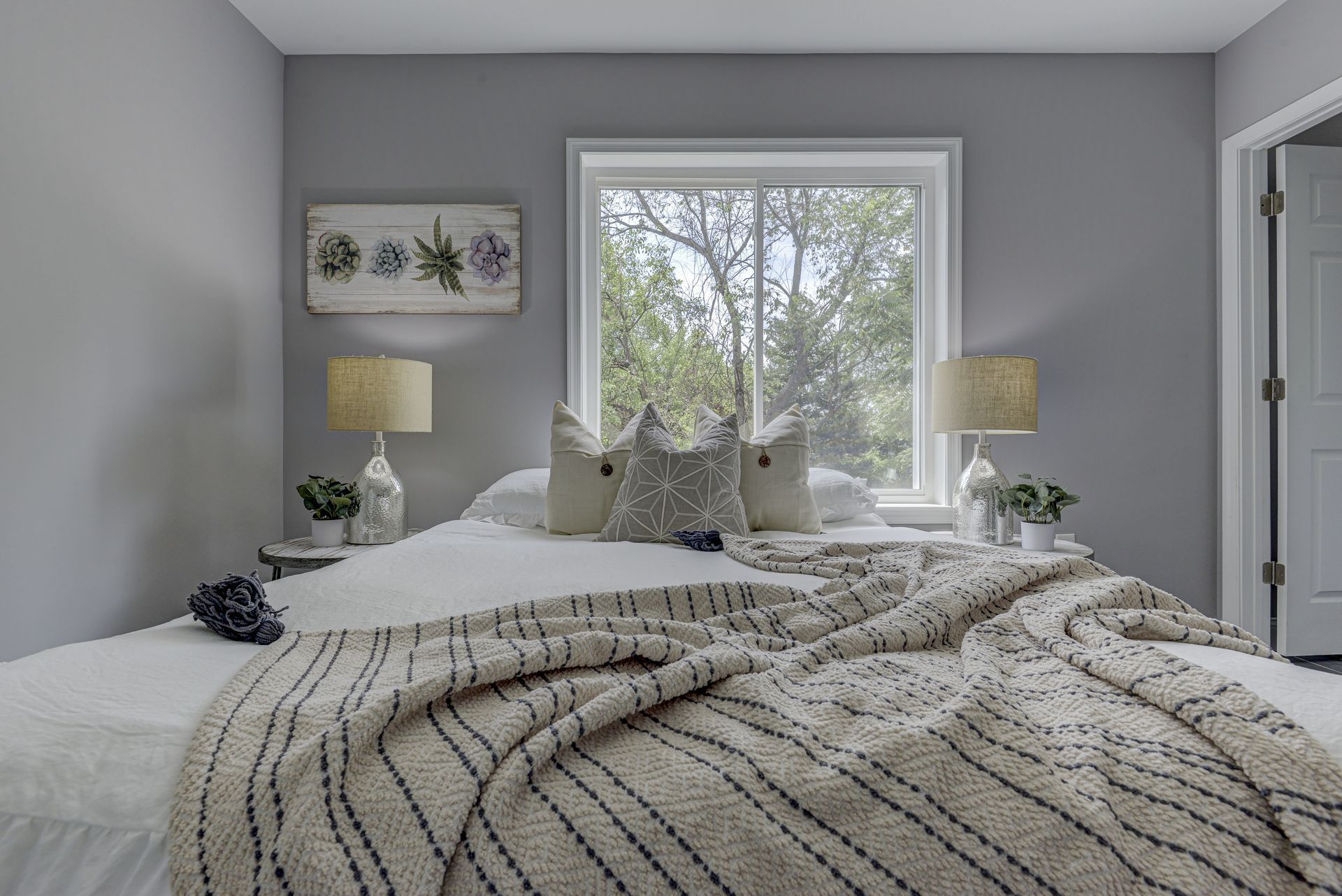 A bedroom with a bed , lamps , a window and a painting on the wall.
