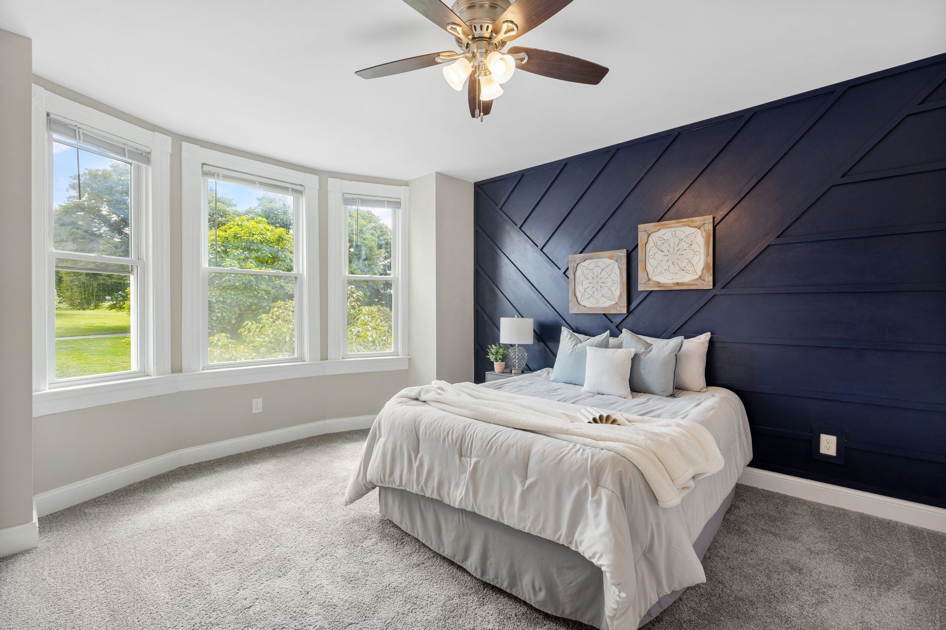 A bedroom with a bed , ceiling fan , and lots of windows.