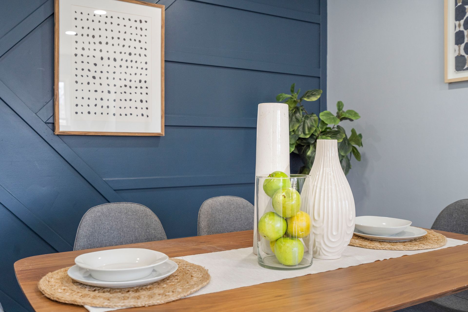 A dining room table with plates , bowls , vases and apples on it.