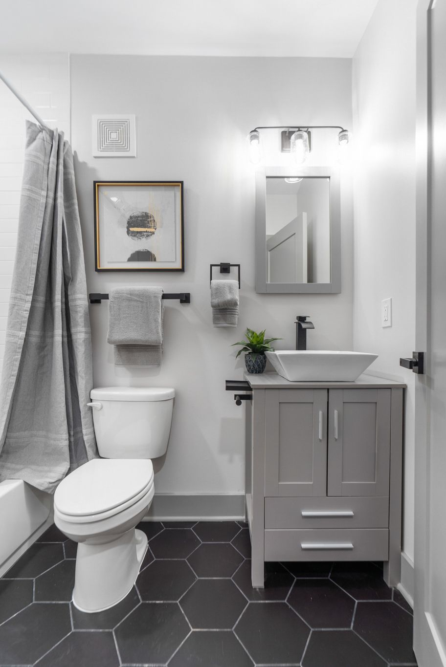 A bathroom with a toilet , sink , mirror and shower curtain.