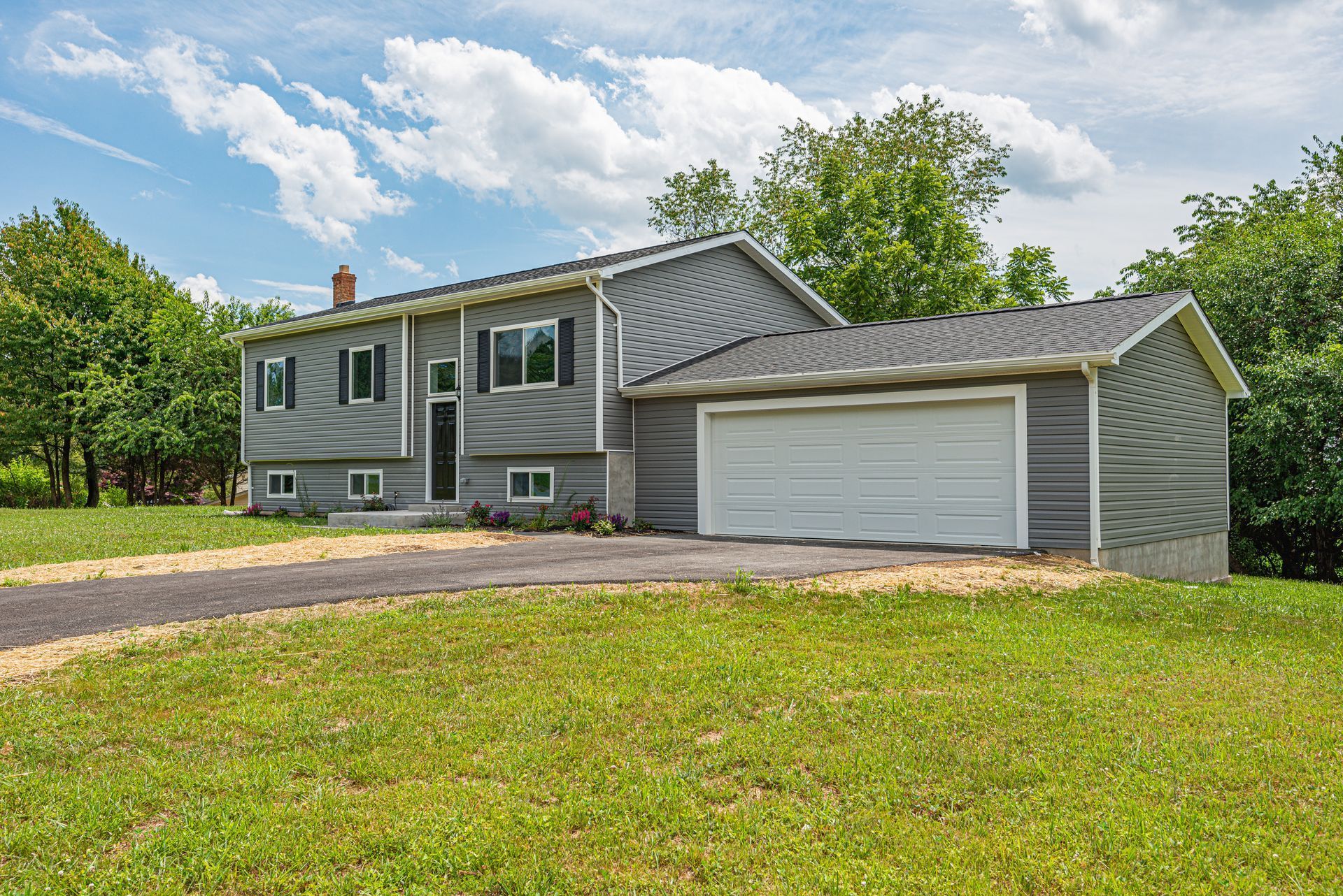 A house with a garage and a driveway is sitting on top of a lush green field.