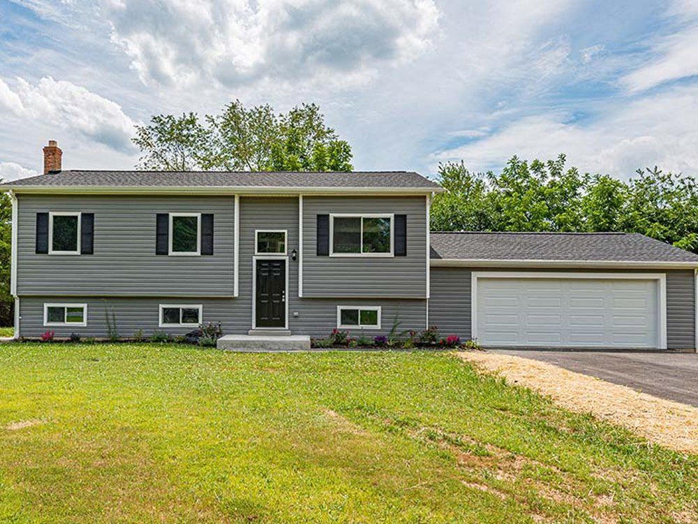 A large gray house with a garage and a large lawn in front of it.