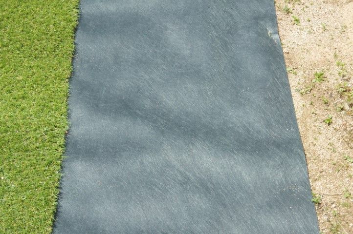 Green turf next to a section of gray landscaping fabric, on sandy ground.