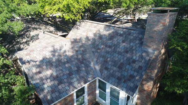 An aerial view of a house with a roof and chimney surrounded by trees.