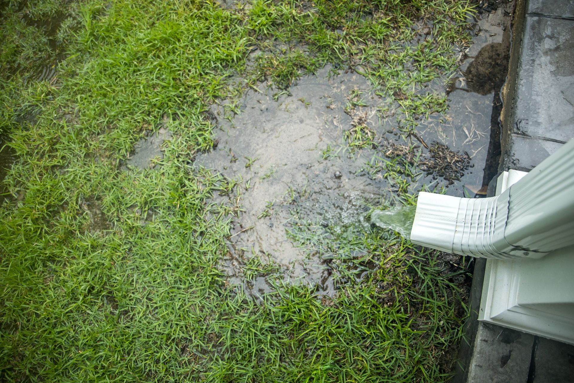 A gutter is draining water into a muddy yard.