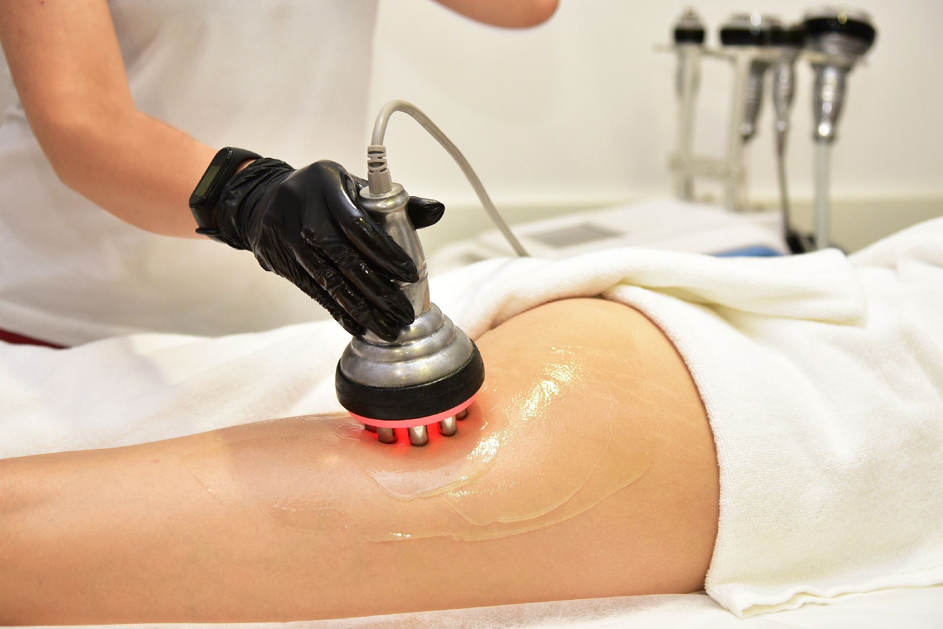 Una persona recibe un tratamiento de contorno corporal en el muslo. Una mano enguantada sostiene un dispositivo de terapia de luz roja.